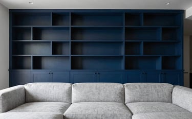A high-end North American living room interior featuring custom-built integrated shelving and a modern minimalist sofa. The palette is dominated by dark blue and light grey, creating a sophisticated and inviting atmosphere with natural sunlight.
