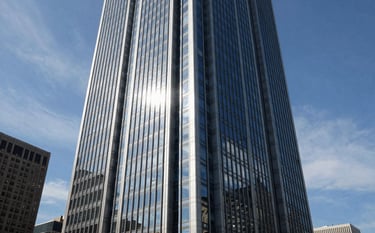 A high-angle architectural photograph of a sleek glass skyscraper in a major North American financial district, reflecting the clear blue sky and thin wisps of clouds, symbolizing corporate transparency and height, professional and authoritative tone, light grey and dark blue palette.