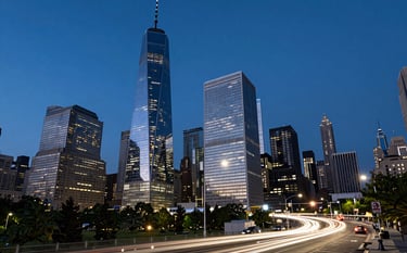 A twilight long-exposure photograph of a global financial hub's architecture, capturing the movement of light in a bustling North American metropolis, emphasizing a sense of international reach and constant motion, dominated by dark blue and near white tones.