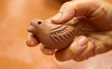 ceramista sosteniendo un pequeño silbato artesanal de barro marrón con tallados detallados.