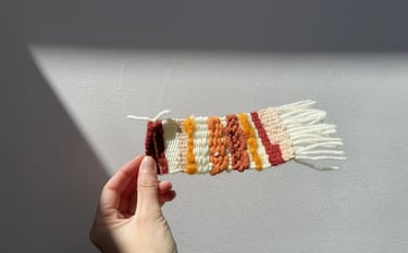 tapiz tejido, con texturas de hilo en tonos naranja, rojo y crema.