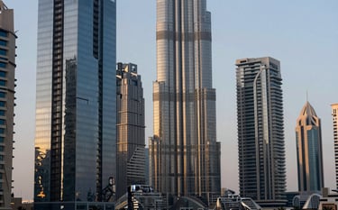 A high-end urban architectural scene representing a fusion of Dubai and Lisbon aesthetics. Gleaming glass structures reflecting a soft sunset in shades of slate gray and ocean blue. Sophisticated and high-wealth atmosphere.