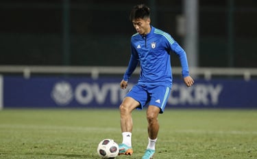 Action shot of a young player in #8FAABF blue training gear, focusing on the ball during an evening practice session under stadium lights. Professional, high-performance aesthetic.