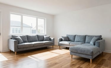 Interior photography of a bright, spacious modern home. A sunlit living room with ice white walls and minimalist soft blue-grey furniture. The hardwood floor is polished and spotless. The atmosphere is fresh, airy, and professional.