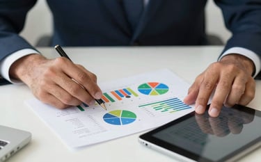 Close-up of hands working on a strategic marketing plan with colorful charts and a digital tablet on a clean white desk. Professional Brazilian corporate setting, bright lighting, colors including green and dark blue.