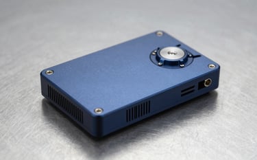 A sophisticated, custom-engineered electronic device prototype resting on a clean metallic surface. The device features high-quality finishes in dark blue tones (#0D1B2A) and precision-machined parts. The lighting is sharp and technical, emphasizing the device's advanced technological detail and professional craftsmanship.