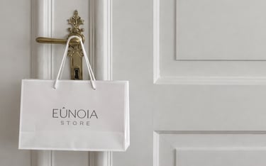 Bolsa de compras de papel de la tienda Eunoia de color blanco colgada en una puerta con paneles.