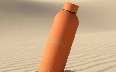 Termo reutilizable de merch eunoia de color naranja colocada en las dunas de arena.