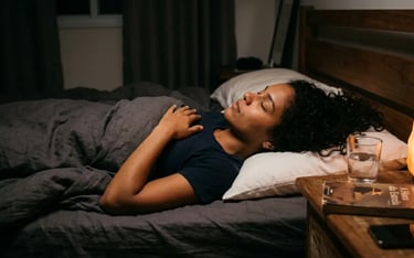 A woman sleeping peacefully in bed with a Himalayan salt lamp on her nightstand.
