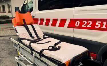 Trage mit orange Kopfstütze vor Krankenwagen mit roten Streifen und Nummern.