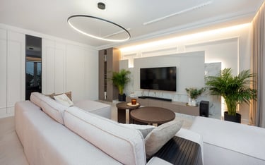 Nowoczesny salon z jasną sofą, stolikiem kawowym, telewizorem na ścianie i dużymi oknami