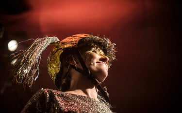 A performer wears a gold tinsel helmet with colorful wire tassels during a creative theater production.