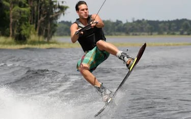 A man in a life jacket performing an athletic jump while wakeboarding on a lake.