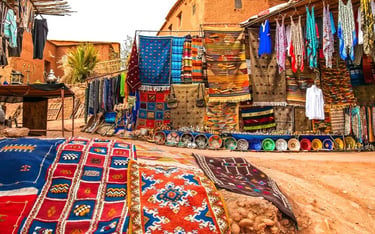 Handwoven colorful Moroccan Berber rugs and textiles displayed at a traditional outdoor market in Morocco.