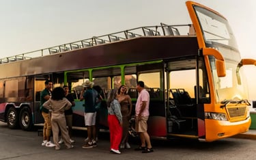 Diverse group of tourists talking next to an open-top double-decker sightseeing bus at sunset.