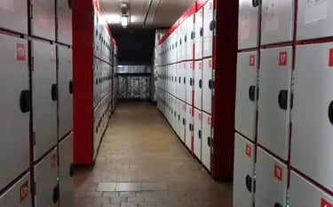Rows of numbered grey and red storage lockers in a secure basement facility or gym locker room.