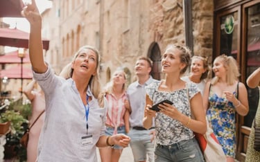 Professional tour guide pointing at historical landmarks for a group of tourists on a European street.