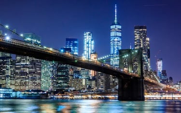 Night view of the Brooklyn Bridge with the illuminated Lower Manhattan skyline and One World Trade Center.