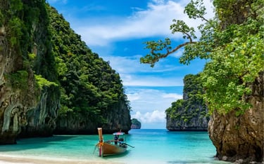 A traditional Thai longtail boat floats on turquoise water by a white sand beach in Phi Phi Islands.
