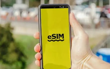 Hand holding a smartphone displaying an eSIM logo on a bright yellow screen outdoors.
