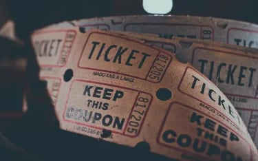 A vintage roll of tan paper raffle tickets and movie coupons with black printed text.