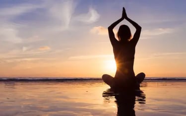 A woman silhouette practicing yoga in a seated pose on the beach at sunset.