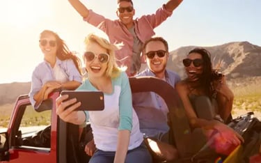 Diverse group of happy friends taking a selfie on a desert road trip in a red convertible.