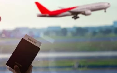 Hand holding a passport and boarding pass at an airport window with a plane taking off.
