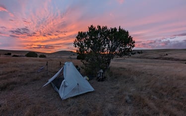 A Hyperlite tent pitched in front of an orange sunset on an open mesa in New Mexico.