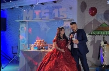 Quinceañera con vestido rojo junto a su padre, mesa de dulces y decoración elegante.