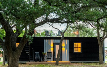 Una pequeña casa contenedor negra con terraza y cubierta.
