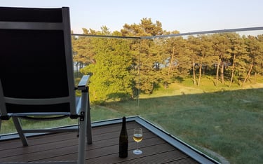 Stuhl mit Blickrichtung Meer steht auf dem Balkon, daneben ein Glas und eine Flasche Wein
