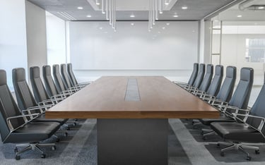 A sleek conference room with a large projection screen, long wooden table, and high-back chairs