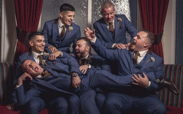 Groom and groomsmen in blue three-piece suits laughing together during a wedding celebration.