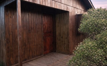 entrada da cabana familiar, de madeira e rústica, com árvores ao redor