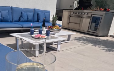 Villa Fay outdoor lounge with a glass of wine on a patio with a blue couch and outdoor kitchen BBQ