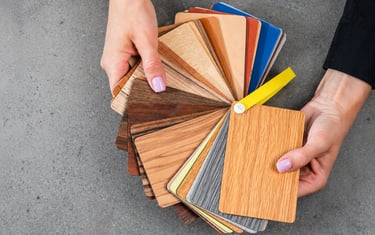 A designer holding a fan of wood laminate samples and color swatches for interior furniture design.