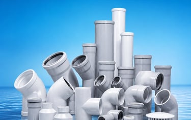 A collection of white and grey PVC plumbing pipes and plastic fittings for sewage drainage systems.