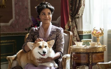 Lady Mary Sharma sentada em uma poltrona luxuosa acariciando o cachorro Newton, o corgi de Kate Shar