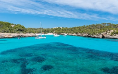Una cala del sur de Mallorca, con aguas turquesas cristalinas, con veleros fondeando