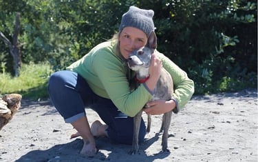 a woman in a green sweater with a dog on the beach