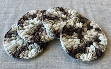 4 stacked puff stitch crocheted drink coasters that are brown, tan and cream colored
