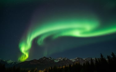 Vibrant green Northern Lights dancing over a dark mountain landscape.