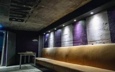 Long leather bench in an underground bunker lounge with industrial concrete walls and purple accents.