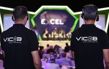 two men in black shirts and headphones are standing in front of a stage