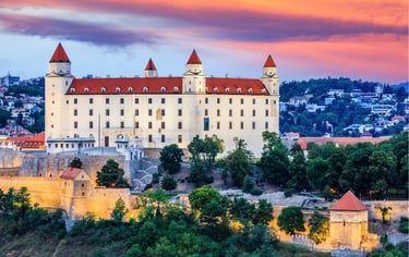 Bratislava Castle at sunset with a vibrant orange and purple sky over the white hilltop fortress in Slovakia.