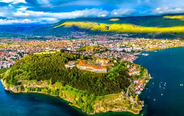 Aerial view of Ohrid city, Samuel's Fortress, and the deep blue Lake Ohrid under a cloudy sky.