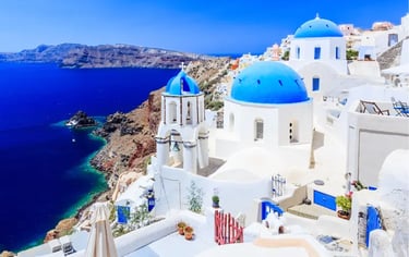 Panoramic view of blue domed churches in Oia, Santorini, overlooking the Aegean Sea.