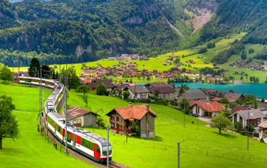 A scenic Swiss train traveling through lush green meadows and a mountain village near a blue lake.