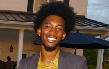 kelvin in a suit and yellow shirt standing in front of a house